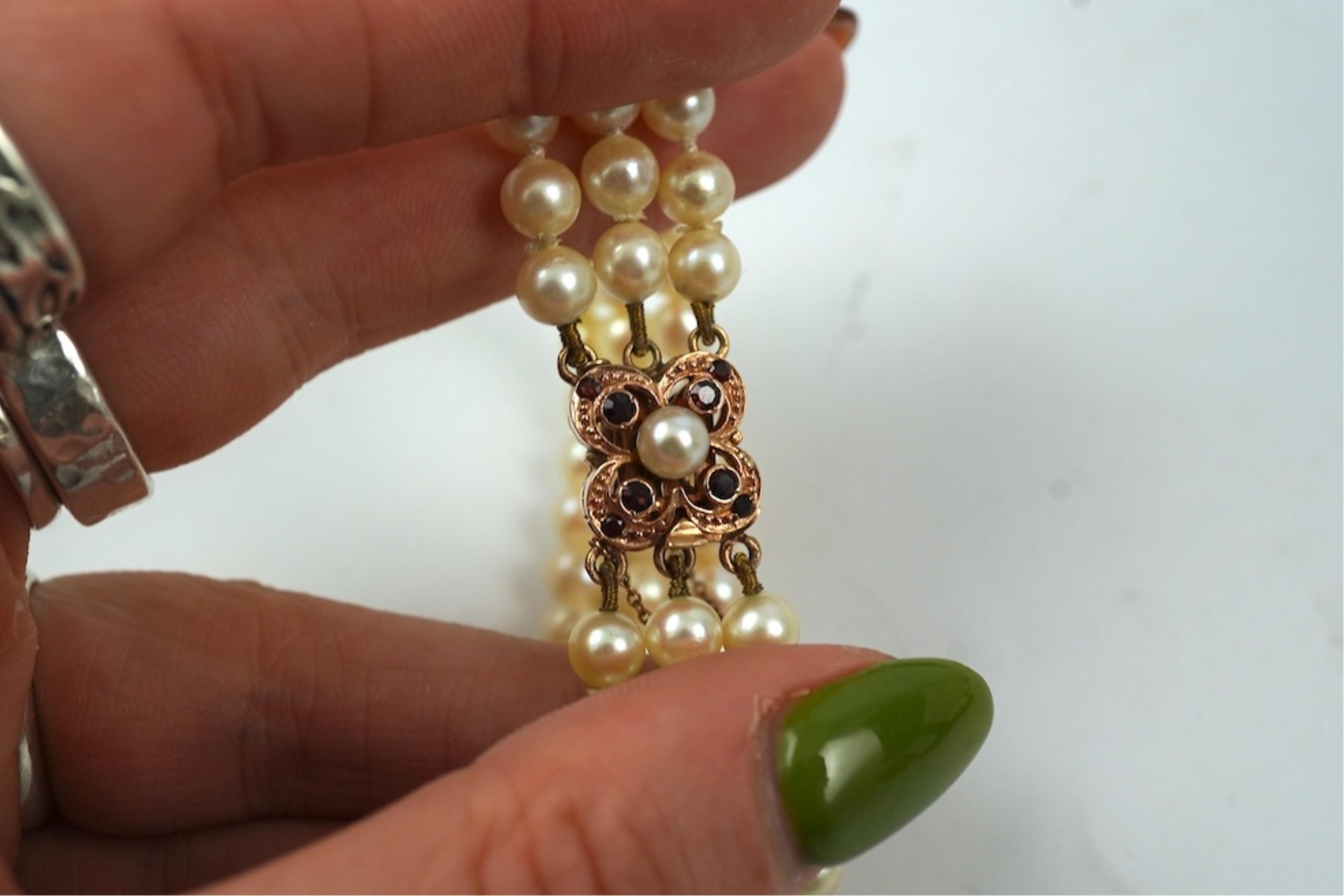 A triple strand cultured pearl bracelet, with a 9ct gold, garnet and cultured pearl cluster set clasp, 16cm.